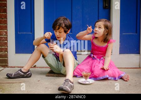 Zwei kleine Kinder sitzen auf einem stoop und essen Schokoladeneis Stockfoto