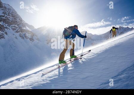 Man Ski Touren bergauf im Wind und von der Sonne hinterleuchtet Stockfoto