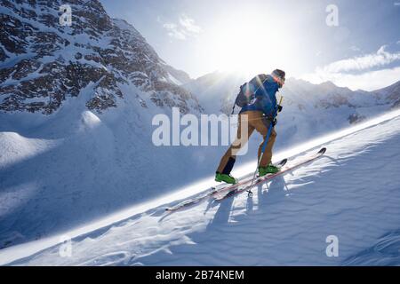 Man Ski Touren bergauf im Wind und von der Sonne hinterleuchtet Stockfoto