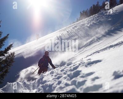 Mann beim Skifahren im Pulverschnee, der von der Sonne beleuchtet wird Stockfoto
