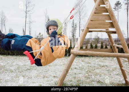 Nahaufnahme eines Jungen, der im Winter auf einer Schaukel draußen schwingt Stockfoto