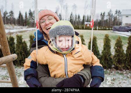 Mutter und Sohn lachen auf einer Schaukel zusammen draußen Stockfoto