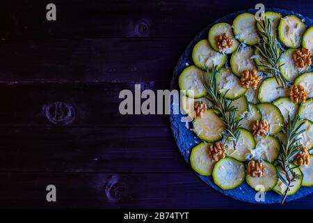 Carpaccio aus Zucchini mit Nüssen und Käse auf dunklem Holzhintergrund Stockfoto