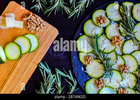 Carpaccio aus Zucchini mit Nüssen und Käse auf dunklem Holzhintergrund Stockfoto