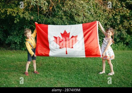 Kaukasische Kinder Jungen und Geschwister, die große kanadische Flagge im Park im Freien halten. Kinder in der Vorschule Freunde Bürger feiern den Canada Day im Sommer Stockfoto