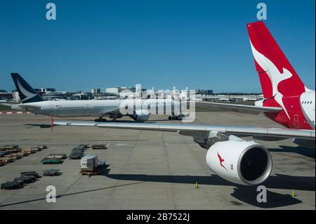 28.09.2019, Sydney, New South Wales, Australien - EIN Passagierflugzeug des Typs Qantas Airbus A380-800 wird am Flugsteig am Kingsford Smith International Airport geparkt, während ein Flugzeug des Typs Cathay Pacific für den Start vorbereitet wird. Qantas ist Mitglied der one World Airline Alliance. [Automatisierte Übersetzung] Stockfoto