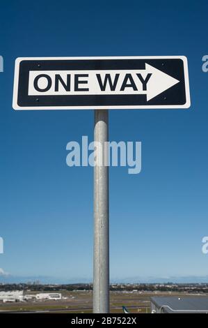 28.09.2019, Sydney, New South Wales, Australien - Einweg-Straßenschild mit Richtungspfeil vor blauem Himmel auf einem Parkdeck an einem Flughafen. [Automatisierte Übersetzung] Stockfoto