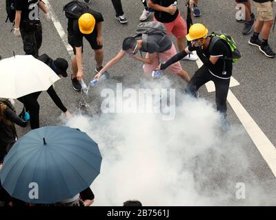 Demonstranten löschen Tränengasbombe, die von der Polizei im Yuen Long District in Hongkong gezündet wurde. Der Polizei wurde vorgeworfen, die Bürger bewusst nicht vor dem Angriff auf unschuldige Zugpassagiere in Yuen Long am 21. Juli 2019 geschützt zu haben. Stockfoto