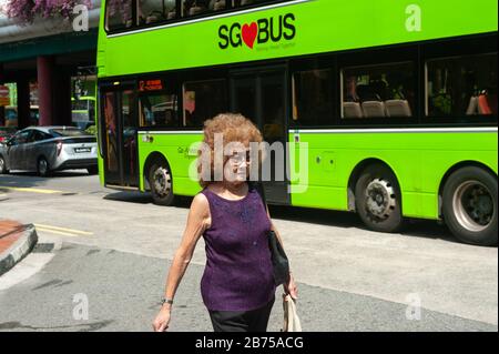 04.04.2018, Singapur, Republik Singapur, Asien - eine ältere Frau überquert eine Straße in Chinatown, während ein Bus im Hintergrund unterwegs ist. [Automatisierte Übersetzung] Stockfoto