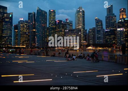 14.12.2018, Singapur, Republik Singapur, Asien - Menschen am Ufer des Singapur-Flusses in der Marina Bay mit der abendlichen Skyline des Geschäftsviertels im Hintergrund. [Automatisierte Übersetzung] Stockfoto