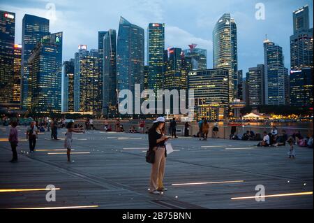 14.12.2018, Singapur, Republik Singapur, Asien - Menschen am Ufer des Singapur-Flusses in der Marina Bay mit der abendlichen Skyline des Geschäftsviertels im Hintergrund. [Automatisierte Übersetzung] Stockfoto