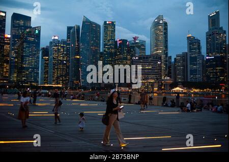 14.12.2018, Singapur, Republik Singapur, Asien - Menschen am Ufer des Singapur-Flusses in der Marina Bay mit der abendlichen Skyline des Geschäftsviertels im Hintergrund. [Automatisierte Übersetzung] Stockfoto