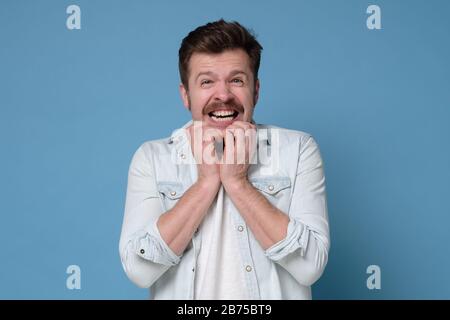 Schockiert erschrocken kaukasischer Mann mit Schnurrbart beißende Nägel in Panik. Studio gedreht Stockfoto