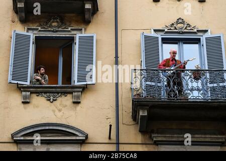 Turin, ITALIEN - 13. März 2020: Ein Mann spielt Gitarre vom Balkon seines Hauses, als ein Junge ihn in der Nachbarschaft von San Salvario während eines in ganz Italien gestarteten Blitzmobs ansieht, um die Menschen zusammenzubringen. Die italienische Regierung hat beispiellose Einschränkungen auferlegt, um die Ausbreitung des COVID-19-Coronavirus-Ausbruchs zu stoppen, und andere Maßnahmen, die die Bewegungen der Menschen nur für die Arbeit, für den Kauf wesentlicher Waren und aus gesundheitlichen Gründen erlaubt sind. (Foto von Nicolò Campo/Sipa USA) Stockfoto