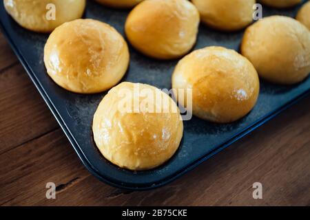 Nahaufnahme von frisch gebackenen hausgemachten Slider Brötchen in runder 12-fach Muffin-Pfanne, fertig zum Essen, auf rustikalem Holztisch Stockfoto