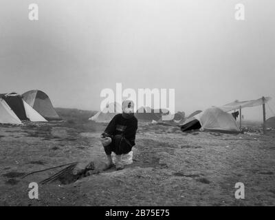 Flüchtlingslager in Idomeni an der Grenze zu Mazedonien. Ein Mann sitzt im Morgengrauen um ein Lagerfeuer. [Automatisierte Übersetzung] Stockfoto