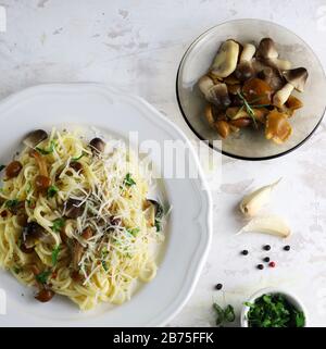Hausgemachte italienische Spaghetti-Pasta mit Pilzen und Sahnesauce. Weißer Hintergrund mit Pilzen, Petersilie und Knoblauch. Draufsicht. Stockfoto