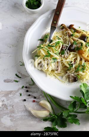 Konzept der italienischen Küche. Hausgemachte Spaghetti-Pasta mit Pilzen und Sahnesauce. Weißer Hintergrund mit Petersilie und Knoblauch. Draufsicht. Stockfoto