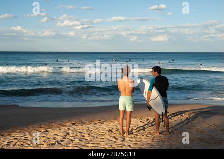 10.05.2018, Sydney, New South Wales, Australien - zwei junge Männer stehen am Manly Beach und blicken aufs Meer, wo Surfer auf die richtige Welle warten. [Automatisierte Übersetzung] Stockfoto