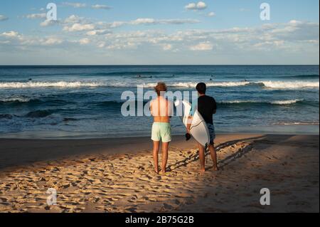 10.05.2018, Sydney, New South Wales, Australien - zwei junge Männer stehen am Manly Beach und blicken aufs Meer, wo Surfer auf die richtige Welle warten. [Automatisierte Übersetzung] Stockfoto