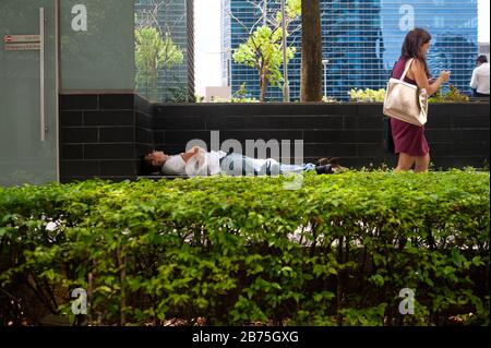 18.04.2018, Singapur, Republik Singapur, Asien - EIN Mann schläft hinter einer Hecke im Geschäftsviertel der Innenstadt von Singapur. [Automatisierte Übersetzung] Stockfoto