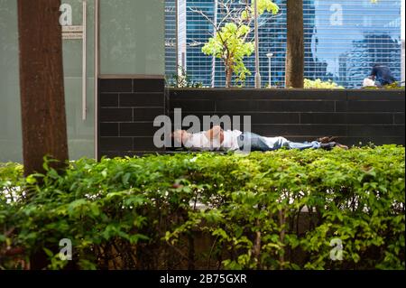 18.04.2018, Singapur, Republik Singapur, Asien - EIN Mann schläft hinter einer Hecke im Geschäftsviertel der Innenstadt von Singapur. [Automatisierte Übersetzung] Stockfoto