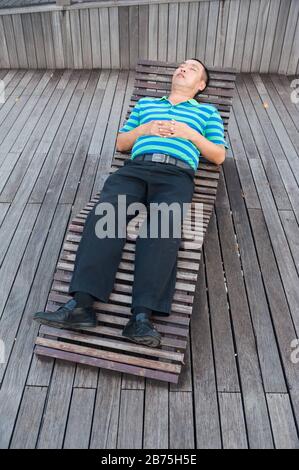 01.03.2018, Singapur, Republik Singapur, Asien - EIN Mann nimmt ein Nickerchen auf einer Holzkecke in der Marina Bay. [Automatisierte Übersetzung] Stockfoto