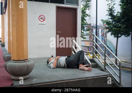 22.03.2018, Singapur, Republik Singapur, Asien - EIN Mann nimmt ein Nickerchen auf dem Boden eines Podiums am Crete Ayer Square im Singapur-Chinatown-Viertel. [Automatisierte Übersetzung] Stockfoto