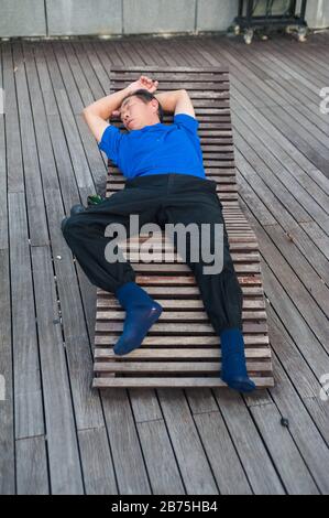 22.03.2018, Singapur, Republik Singapur, Asien - EIN Mann nimmt ein Nickerchen auf einer Holzkecke in der Marina Bay. [Automatisierte Übersetzung] Stockfoto