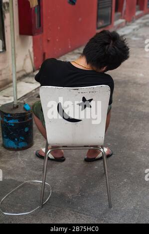 31.03.2018, Singapur, Republik Singapur, Asien - EIN junger Mann sitzt auf einem Stuhl im Chinatown-Distrikt von Singapur und nimmt einen Nickerchen. [Automatisierte Übersetzung] Stockfoto