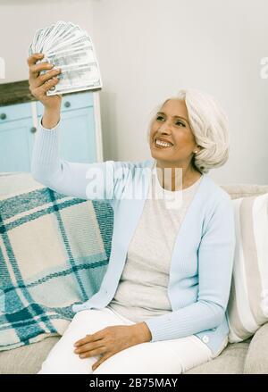 Ältere Frauen Erhielten Dividenden Ältere Frauen, Die Viel Geld In Ihren Händen Halten, Während Sie Auf Sofa Zu Hause Drinnen Sitzen, Getontes Bild Stockfoto