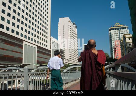 27.01.2017, Yangon, Yangon Region, Republik der Union von Myanmar, Asien - EIN buddhistischer Mönch steht auf einer Fußgängerbrücke und fotografiert das neue Gebäude am Sule Square im Zentrum von Yangon. [Automatisierte Übersetzung] Stockfoto