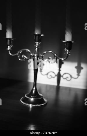 Vintage-Kerzenhalter mit drei Kerzen auf dem Tisch. Schattenreflexion an der Wand. Schwarzweißfoto Stockfoto