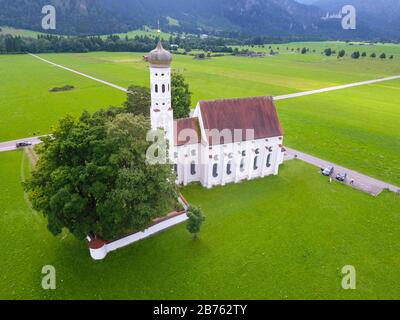 Luftbild zur barocken St.-Coloman-Kirche bei Schwangau in Bayern. Jahrhundert zu Ehren des Heiligen Koloman erbaut. Der Irlandpilger soll im Sommer 1012 auf seiner Pilgerreise ins Heilige Land an diesem Ort angehalten haben. Wegen seiner Lage am Fuße der Schwangauer Berge und der Nähe zum weltberühmten Schloss Neuschwanstein ist die Kirche eine der bekanntesten Sehenswürdigkeiten Bayerns. [Automatisierte Übersetzung] Stockfoto