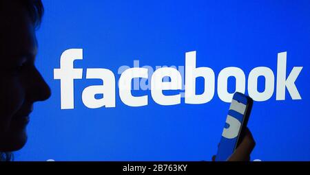 Die Silhouette einer Frau mit einem Smartphone in der Hand ist vor einem Facebook-Logo zu sehen, am 23.03.2016 [automatisierte Übersetzung] Stockfoto