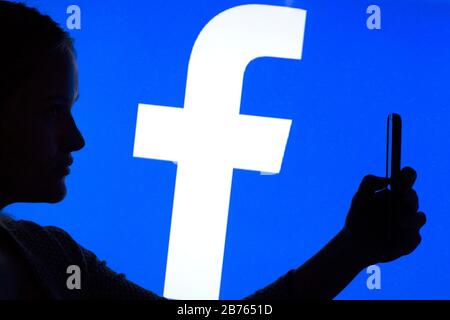 Die Silhouette einer Frau mit einem Smartphone in der Hand ist vor einem Facebook-Logo zu sehen, am 12.01.2016 [automatisierte Übersetzung] Stockfoto