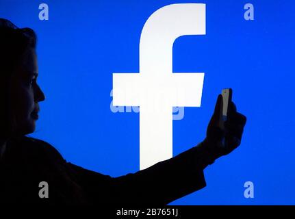 Die Silhouette einer Frau mit einem Smartphone in der Hand ist vor einem Facebook-Logo zu sehen, am 12.01.2016 [automatisierte Übersetzung] Stockfoto