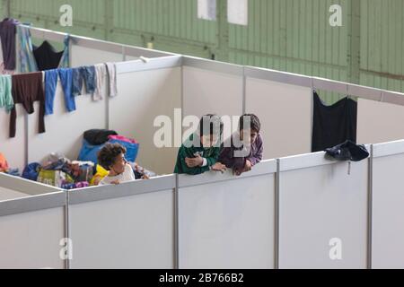 Kinder von Flüchtlingen blicken am 9. Dezember 2015 im ehemaligen Hangar des Flughafens Tempelhof über die Wand eines provisorischen Raumes in einer Notunterkunft für Flüchtlinge. Der Flughafen Tempelhof dient der Stadt Berlin als Notunterkunft für Flüchtlinge. [Automatisierte Übersetzung] Stockfoto