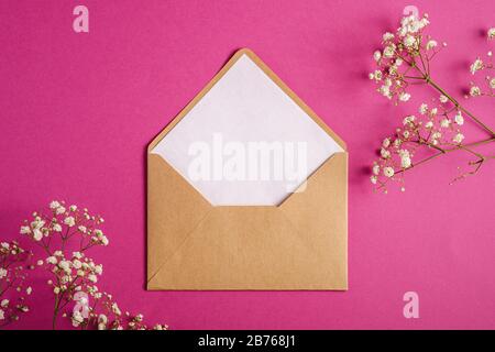 Kraft braune Briefumschläge mit weißer leerer Karte, Zigeuner-Lila-Blumen, violett-rosa Hintergrund, verspottelter Leerbrief Stockfoto