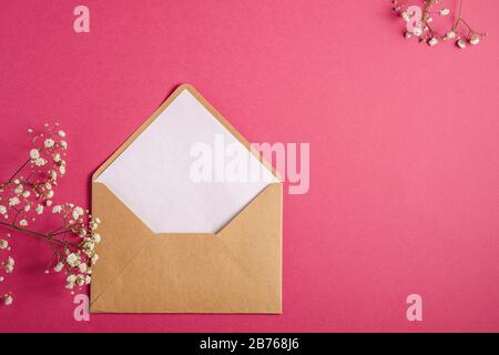 Kraft braune Briefumschläge mit weißer leerer Karte, Gypsophila-Blumen, rot-rosa Hintergrund, Mockup-Vorlage Stockfoto