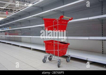 Einkaufswagen mit leeren Körben gegen leere Regale im Lebensmittelgeschäft Stockfoto