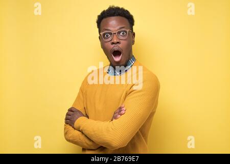 Junger afroamerikanischer Mann in gelbem Pullover in Schock, halten den Mund weit offen Stockfoto