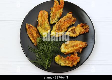 Gebratene Zucchini-Blumen befinden sich auf einer dunklen Platte auf weißem Grund, Draufsicht Stockfoto