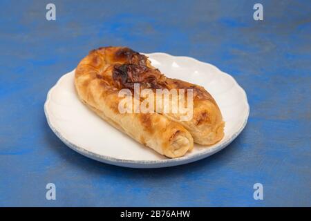 Traditionelle bulgarische Käsekuchen Banitsa aus Filoteig auf weißem Teller auf blauem Grund Stockfoto