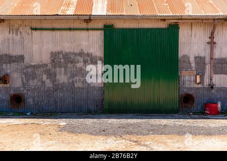 Metallische Scheune oder Pfandschiebetür in grüner Farbe mit einem alten halbgeschnittenen roten Fass Stockfoto