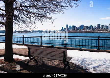 Montreal, Quebec, Kanada - März 2020 - Blick auf den Bezirk Vieux Montreal und den Fluss Saint Laurent im Winter. Querformat mit Bank und Baum Stockfoto