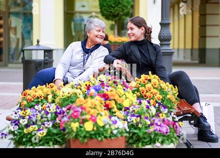 Ein junges Mädchen spricht mit einer älteren Frau, die auf einer Bank unter Blumen sitzt Stockfoto