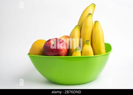 Eine leuchtend grüne Plastikschale mit kunstvoll angeordneten frischen und reifen Früchten wie Äpfeln, Bananen, Orangen und anderen auf einem einfarbigen weißen Hintergrund. Stockfoto