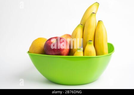 Eine leuchtend grüne Plastikschale mit kunstvoll angeordneten frischen und reifen Früchten wie Äpfeln, Bananen, Orangen und anderen auf einem einfarbigen weißen Hintergrund. Stockfoto