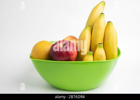Eine leuchtend grüne Plastikschale mit kunstvoll angeordneten frischen und reifen Früchten wie Äpfeln, Bananen, Orangen und anderen auf einem einfarbigen weißen Hintergrund. Stockfoto